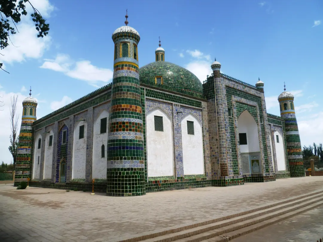 Tiled mausoleum with a green dome and four corner minarets under a blue sky.