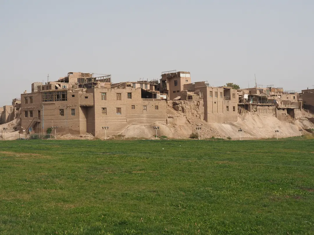 Mud-brick houses of an old town standing on a loess cliff above a green field.