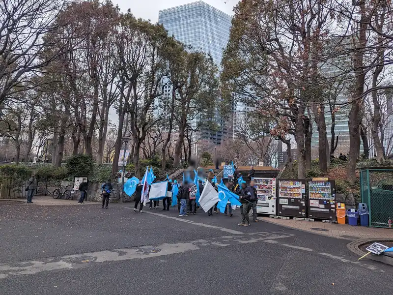 Small group of marchers with pale blue flags and a banner setting off along a park road.