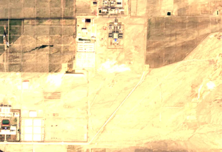Edge of a desert under pale haze: bare ground, straight field boundaries, a track running down to the right, and a few small enclosed plots. More than half of this view is washed out to near-white.