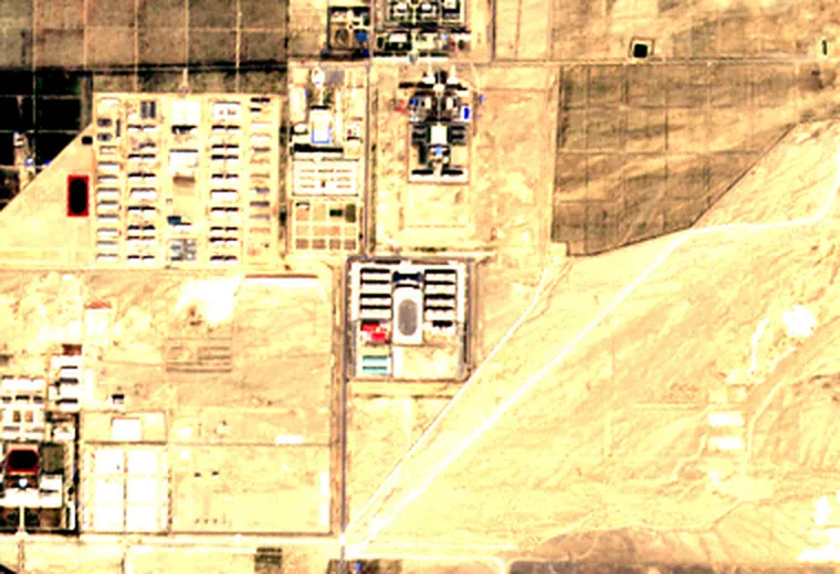 The same ground four years later: a large compound of rows of long identical buildings behind a boundary line, and a second, smaller compound of the same kind below it and to the right.