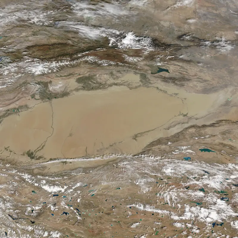 Satellite view of a pale sand basin ringed by snow-streaked mountain ranges.